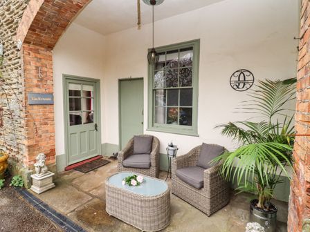 An outdoor covered seating area with two wicker chairs a matching table and a potted palm at The Tack Room in Lydney