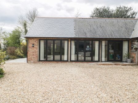 A gravel driveway in front of a building with large windows and a slate roof at The Courtyard - Hilltop Barn in Winterborne Zelston near Wareham