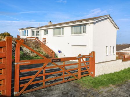 A white house with large windows and a wooden gate at Windy Ridge in Trearddur Bay
