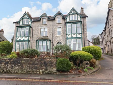 A stone building with green and white framed windows surrounded by bushes and a stone wall at Inglewood Court in Arnside