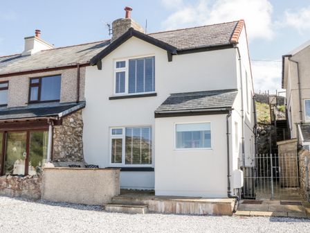An exterior view of a two-story semi-detached house with white walls and multiple windows at 4 Anglesey Road in Llandudno