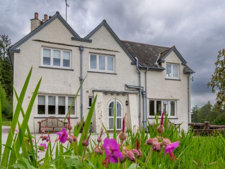 Front view of a two story house with white walls and multiple windows with flowers in the foreground at Hazelseat House in Graythwaite near Ulverston