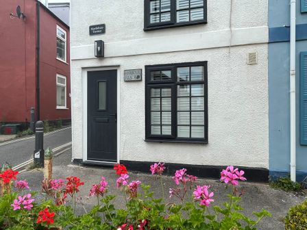 Front of a white building with black door and window frames flowers in front at Harbour Reach Brewers Quay Harbour