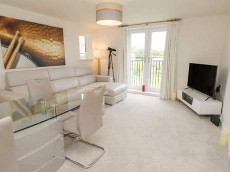 A living room with a glass dining table chairs a beige sofa a floor lamp a telescope a TV on a stand and double doors with curtains at The Green in Whitby