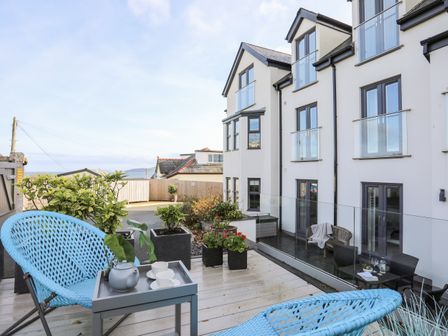 A patio with two blue chairs a small table with a teapot and cups and potted plants at Steps Away in Benllech