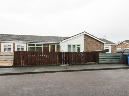 A single story house with brick and white panel exterior a tiled roof green window frames and a wooden fence in front at Swale Cottage in Beadnell