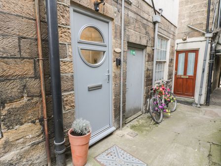 A narrow outdoor alley with three doors two bikes decorated with flowers and a plant in a pot at 1 Burns Yard in Whitby