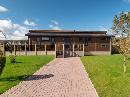 A wooden house with a paved pathway and green lawn at Lobster Lodge in Runswick Bay