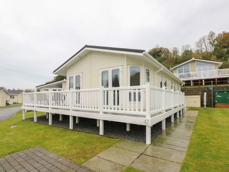 An exterior view of a beige lodge with white railings on a raised deck at Cwtch Lodge 42 Stepaside near Wisemans Bridge