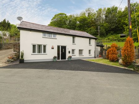 A white two-story house with a black door and multiple windows surrounded by trees at Bwthyn Bach Gwyn in Penrhyndeudraeth