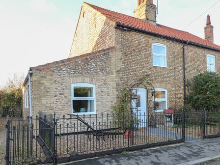 A stone cottage with red roof tiles and white windows behind a black metal fence at Rose Cottage in Downham Market