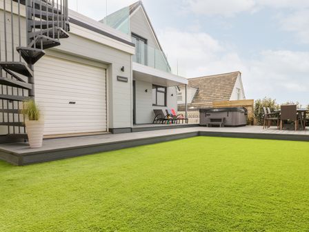 An outdoor area with artificial grass a deck with chairs a hot tub and a spiral staircase at Pepperpots in Mawgan Porth