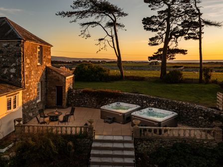 Two hot tubs on a stone patio next to a stone house with a table and chairs at Bennar Fawr in Dyffryn Ardudwy