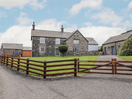 A stone farmhouse with wooden gates and a grassy yard at Plas Iolyn in Pentrefoelas near Betws-Y-Coed