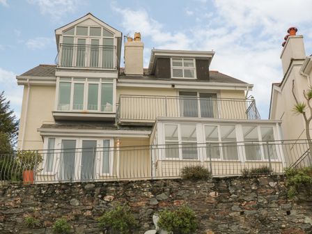A multi-story house with balconies and large windows behind a stone wall and metal railing at The Keel Row in Salcombe
