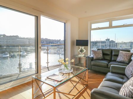 A living room with black leather sofas a glass coffee table with flowers and a lamp by the window at Harbourside Haven Apartment 3 in Weymouth
