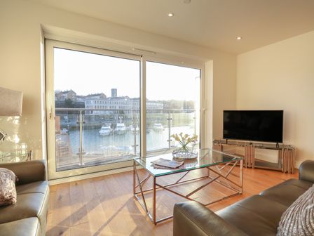 A living room with leather sofas glass coffee table and a television near large windows overlooking boats at Harbourside Haven Apartment 4 in Weymouth