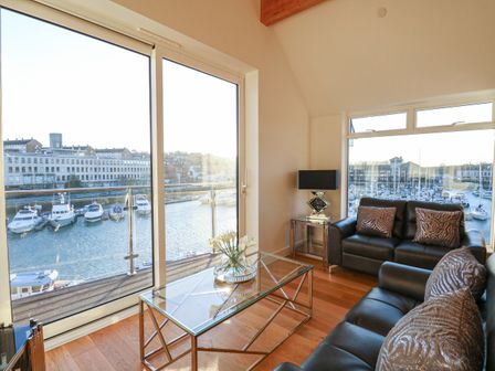 A living room with leather sofas glass coffee table and large windows overlooking a marina at Harbourside Haven Penthouse 1 in Weymouth
