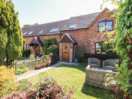 A brick house with wooden doors and skylights with a garden furnished with rattan chairs and surrounded by plants at 3 Mount Pleasant in Pershore