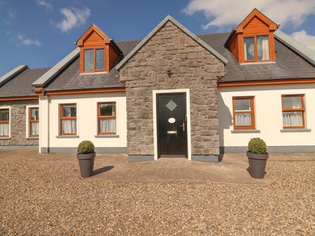 Exterior of a stone and white cottage with black door and two potted plants at Cherry Blossom Cottage in Quilty County Clare