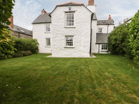 A white stone house with multiple windows and a grassy yard surrounded by bushes at Great Western Farmhouse in Crantock