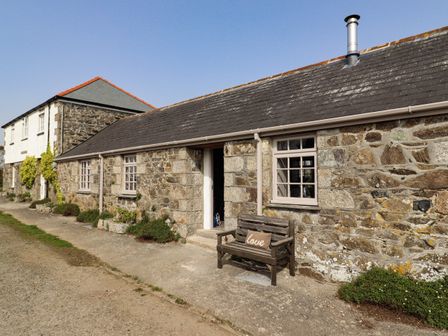 A stone cottage exterior with windows and a bench with a pillow outside at The Roost in Porthallow