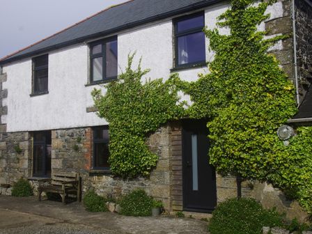 A stone and white plaster house with ivy climbing the walls bench outside and several windows at The Bower in Manaccan near St Keverne