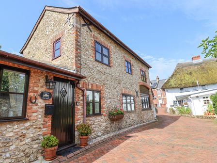 A stone cottage with black framed windows and a black door on a brick paved street at Stable Cottage Colyton