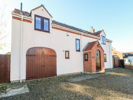 A detached house with white walls brown windows and doors and a small brick porch at Anvil Cottage in Appleton Wiske