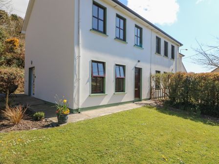 The exterior of a two story house with white walls and green window frames with a garden and potted plants at 1 Closheen Lane Rosscarbery County Cork