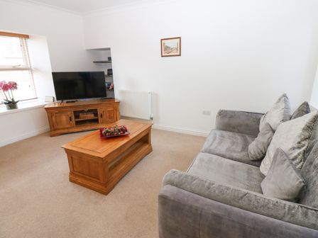 A living room with a gray sofa wooden coffee table and wooden TV stand with a television at 2 Eden Lodge in Kirkby Stephen