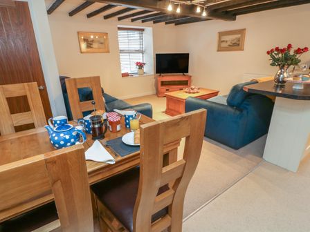 A dining area with wooden chairs and a table set with a teapot cups and breakfast items next to a living room with blue sofas a wooden coffee table and a television at 3 Eden Lodge in Kirkby Stephen