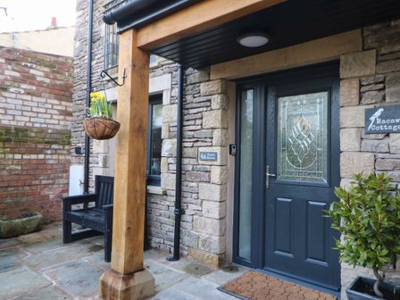 A stone entrance with a blue door and a wooden post supporting a roof at Macaw Cottages No 4A in Kirkby Stephen