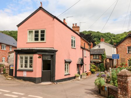A street view with a pink two-story building and a narrow road with plants and signs at Old Bridge Post Office in Roadwater