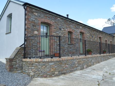An exterior view of a stone building with light green doors and windows a black metal railing and flower pots on the ledge at Cwrt y Wennol in Salem near Clydach