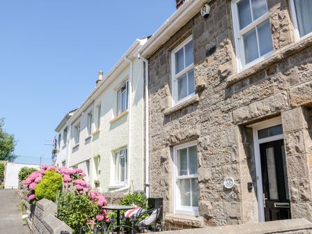 A row of terraced houses with stone and white facades with flowers and a small table with chairs outside at Mazey Cottage in Penzance