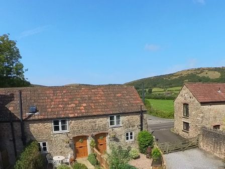 Two stone houses with tiled roofs and wooden doors surrounded by greenery and hills at Wavering in Compton Bishop near Axbridge