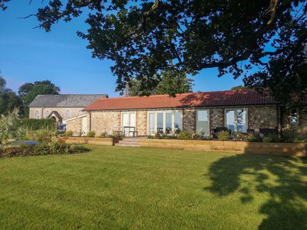 A stone house with a red tiled roof and glass doors surrounded by a garden and lawn at The Cosy Cowshed in Dalwood