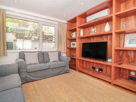 A living room with gray sofas a large wooden shelving unit with a television and decorative items at George Cottage in Dartmouth
