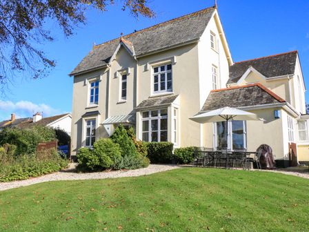 An exterior view of a two story house with gravel pathways greenery and outdoor dining table with umbrella at Victoria Lodge in Kingsbridge
