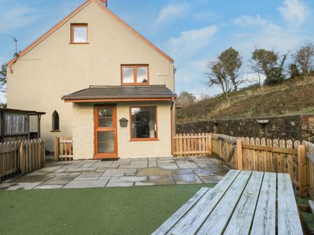 A fenced patio area with a wooden picnic table in front of a house at Nant Moel Isaf Farm in Rhydyfro near Pontardawe