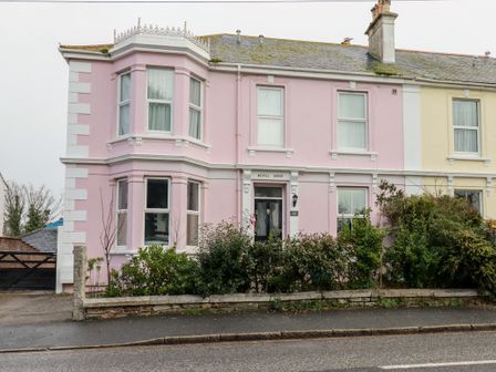 A pink two-story house with bay windows and plants in front at Melvill House in Falmouth
