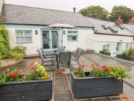 An outdoor patio with a table, six chairs, an umbrella, flower boxes, and a white house with blue window frames at Y Beudy in Crosswell, Eglwyswrw near Newport, Pembrokeshire