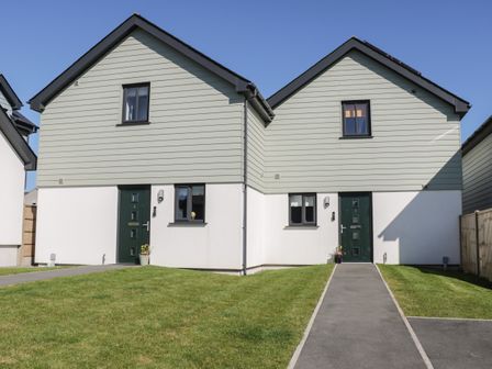 A semi detached house with two green doors and windows and a lawn in front at 3 Parc Delfryn in Brynteg near Benllech