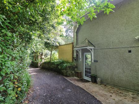 A gravel pathway beside a house entrance with a small canopy and plants at Chydour in Penzance