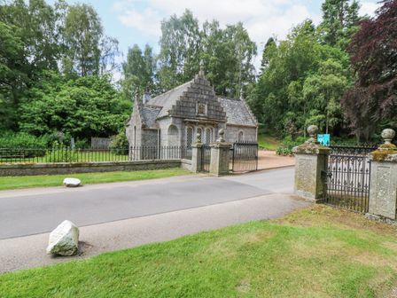 A stone gatehouse with iron gates beside a road and surrounded by trees and grass at East Lodge Crathes Castle near Banchory