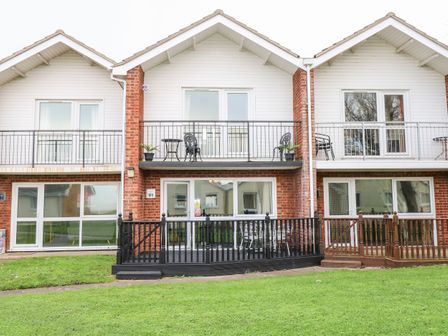 A two-story brick and white siding building with balconies and patios overlooking a grassy area at 91 Waterside Park in Lowestoft