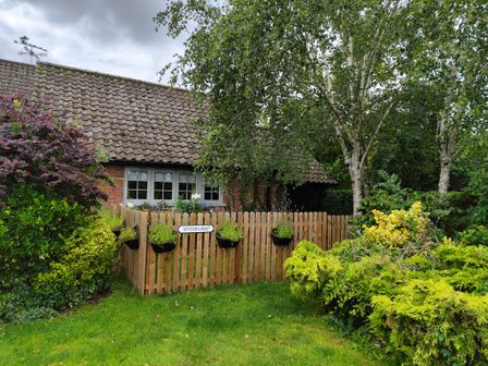 A wooden fenced garden area with plants in front of a house with tiled roof and windows at Hunters Lodge in Great Moulton near Long Stratton