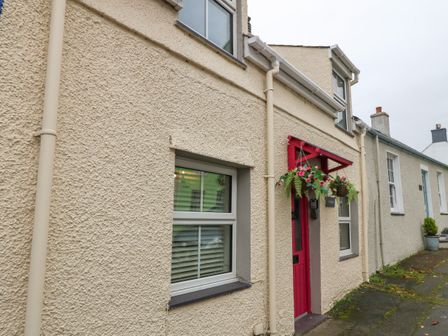 A street view of houses with textured cream walls and a red door with hanging flower baskets at Angorfa in Beaumaris