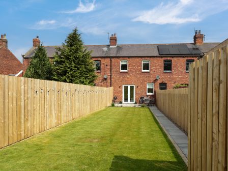 A backyard with grass lawn and wooden fences on each side at The Miners Cottage in Scremerston near Berwick-Upon-Tweed
